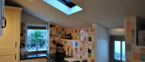 A kitchen with white cabinets, a black countertop, a skylight, and colorful tiles.