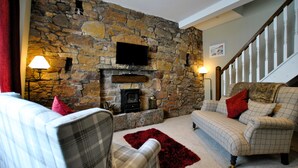 A cozy living room with a stone wall, a fireplace, a television, and a staircase. - 54 On the Rocks- characterful coastal cottage (Anstruther)