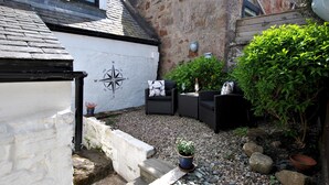 A courtyard with a white wall featuring a compass rose, outdoor seating, and a small garden area with potted plants and rocks. - 54 On the Rocks- characterful coastal cottage (Anstruther)