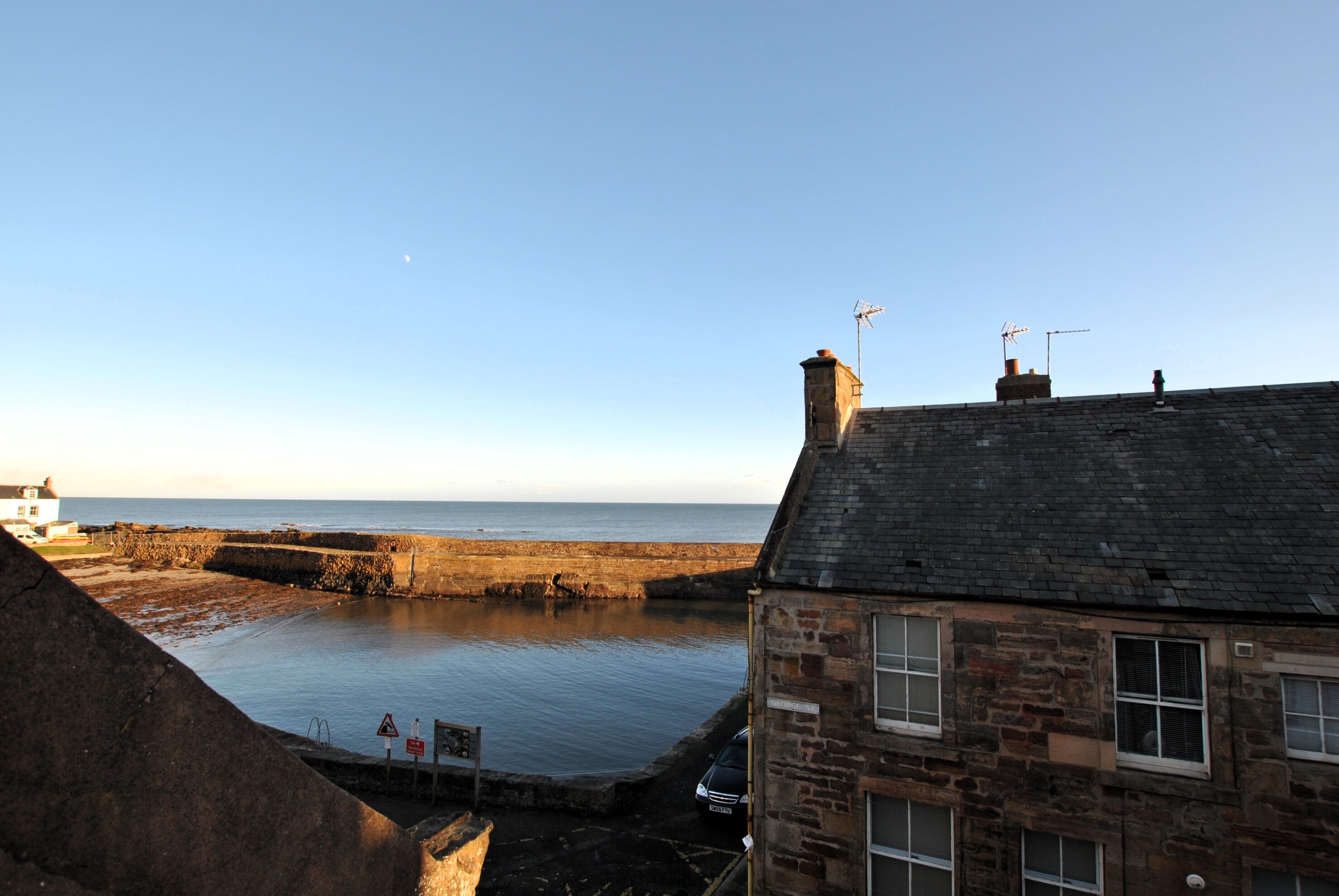 A stone building with a chimney, a view of the sea, and a clear sky.