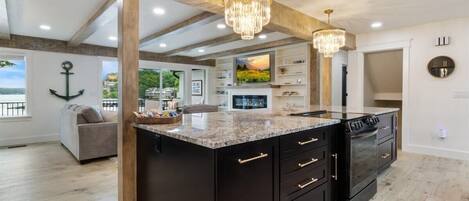 A modern kitchen with a large island, black cabinetry, and a chandelier.