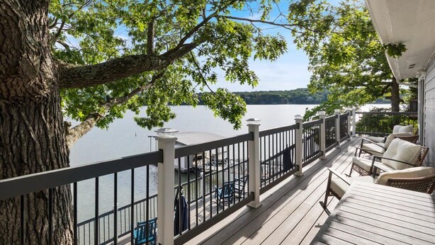 A wooden deck with outdoor furniture, a railing, and a view of a lake.
