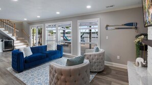 A spacious living room with a blue sofa, a beige armchair, and a patterned rug. A staircase leads to an outdoor area with a slide.
