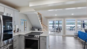 A modern kitchen with stainless steel appliances, a built-in oven, and a coffee machine. There is a staircase leading to a balcony with a view of the lake.
