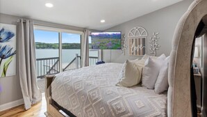 A bedroom with a large bed, a view of a lake, and a painting of flowers.