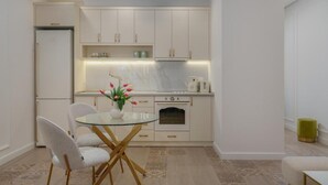 A compact kitchen with white cabinets, a glass dining table, and a small oven. - Prime City Residence by Sweet Home (Yerevan)