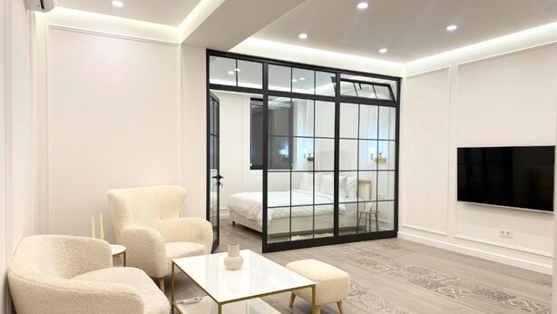 A modern hotel room with a large bed, a TV, a glass partition, and a seating area with a table and chairs. - Prime City Residence by Sweet Home (Yerevan)