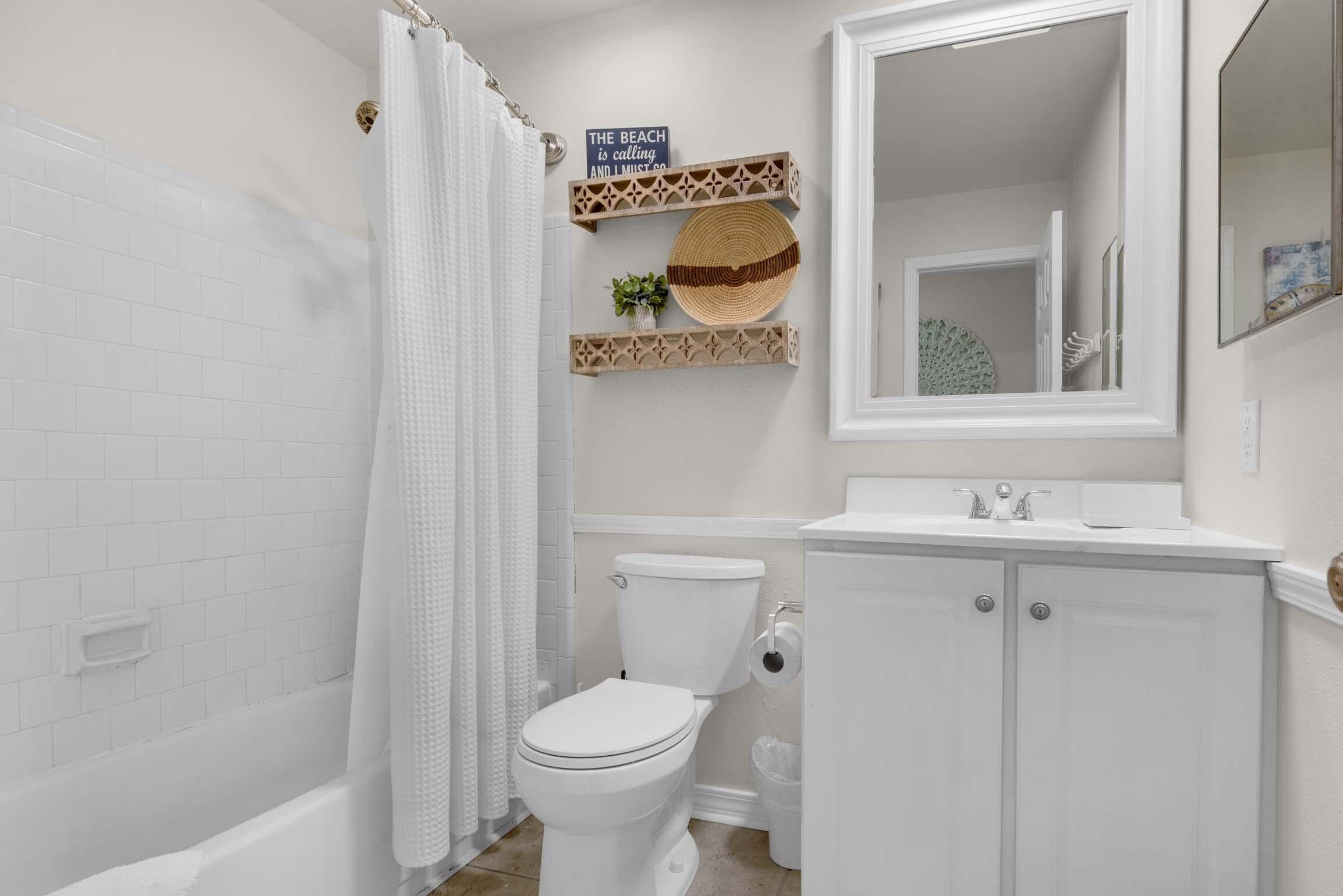 A bathroom with a white toilet, a shower curtain, a sink with a mirror, and decorative shelves.