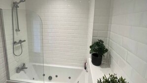 A modern bathroom with a glass-enclosed shower, white tiled walls, and a potted plant.