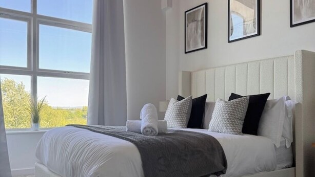 A bedroom with a large window, a bed with white bedding, and a gray throw blanket.