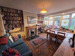 A cozy living room with a fireplace, bookshelves, a dining area, and a large window.