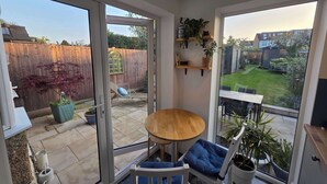 A patio with a table and chairs, a sliding glass door, a wooden fence, and a garden view. - Peaceful 3BDR Retreat by Epping Forest Chingford (Greater London)