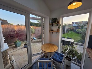 A patio with a table and chairs, a sliding glass door, a wooden fence, and a garden view.