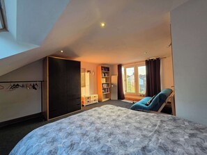 A bedroom with a bed, a wardrobe, a bookshelf, a desk, and a window with curtains.