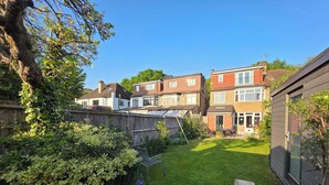 A residential backyard with a lawn, a wooden fence, and houses in the background. - Peaceful 3BDR Retreat by Epping Forest Chingford (Greater London)