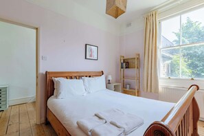 A neatly made bed with white linens and towels, a wooden headboard, a bedside table with a lamp, and a window with curtains.