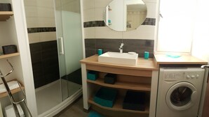 Ein Badezimmer mit Duschkabine aus Glas, einem Waschbecken mit Spiegel darüber und einer Waschmaschine.