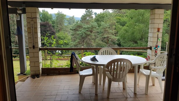 Eine Terrasse mit einem runden Tisch, vier Stühlen, einem Holgitter und Blick auf eine bewaldete Landschaft.