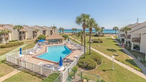 A pool area with lounge chairs and umbrellas, surrounded by a fence, with a view of the sea and palm trees. - 🐾️Pet Friendly ~ Beach View - Pool ~ Blue Surf 17B☀️ (Miramar Beach)
