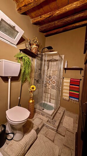 Un baño con inodoro, ducha y un estante decorativo con una estatua y un jarrón.