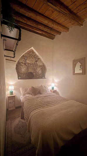 Un dormitorio con cama, dos lámparas de noche, un revestimiento de pared de piedra y una lámpara colgante.