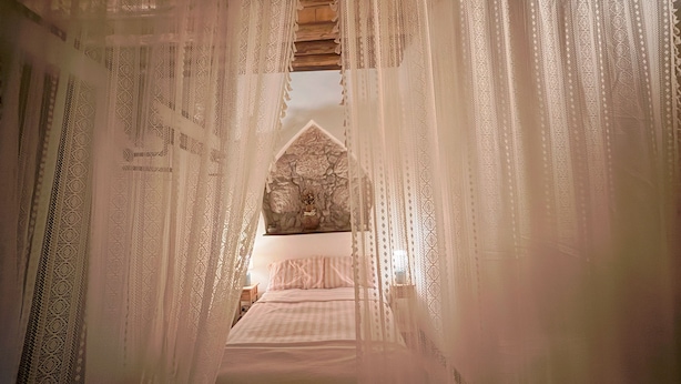 Une chambre à coucher avec un lit à baldaquin, un mur en pierre et une table de chevet avec une lampe.