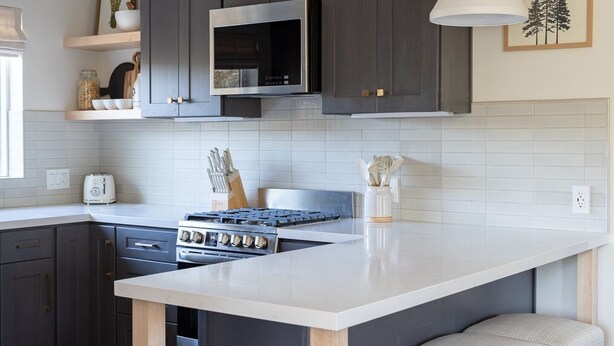 A modern kitchen with dark cabinets, a white island with bar stools, a gas stove, and pendant lighting.