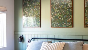 A bedroom with a bed, a wall-mounted light, and two framed floral artworks.
