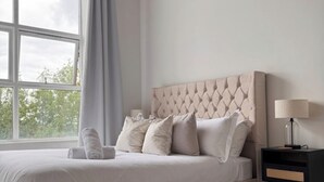 A neatly made bed with a tufted headboard, a bedside lamp, and a view of trees through a window.
