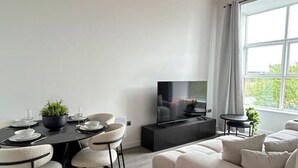 A modern living room with a dining area, a flat-screen TV, and a sofa.