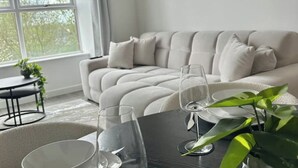 A modern living room with a light-colored sofa, a glass coffee table, and a view of greenery outside.