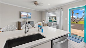 A modern kitchen with a built-in dishwasher, a large sink, and a dining area with a view of the street. - 🌴BEACH FRONT- Chair Service-Capri by the Gulf 122 (Destin)