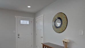 Un couloir avec deux portes blanches, une console en bois sur laquelle est posé un vase de fleurs, et un miroir décoratif accroché au mur.