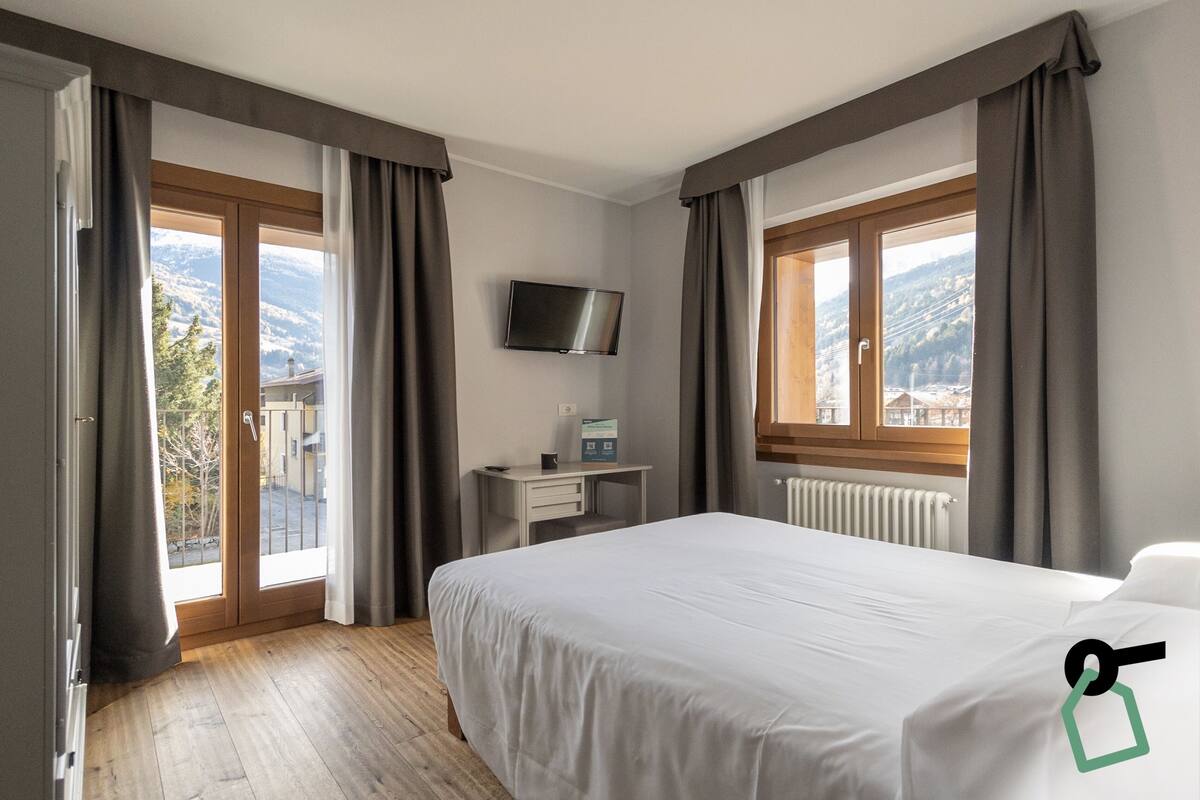 A hotel room with a bed, a desk, a TV, and a window with curtains.