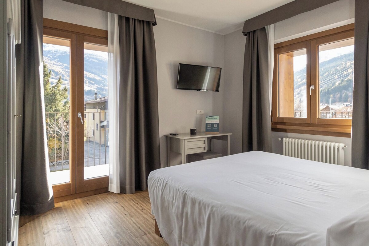 A hotel room with a bed, a desk, a TV, and a window with curtains.
