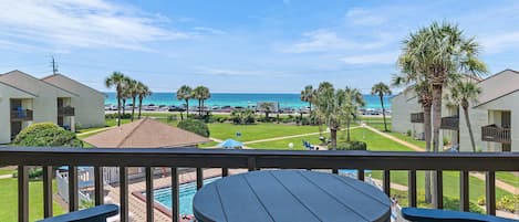 A balcony with a view of a swimming pool, palm trees, and a beach.