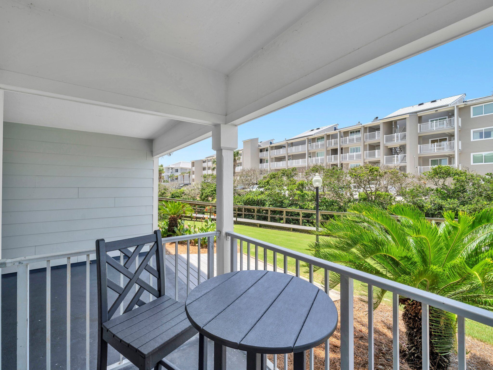 A balcony with a round table and two chairs, overlooking a well-maintained lawn and a multi-story building with balconies.