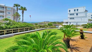 A coastal hotel with a grassy lawn, palm trees, and a view of the ocean.