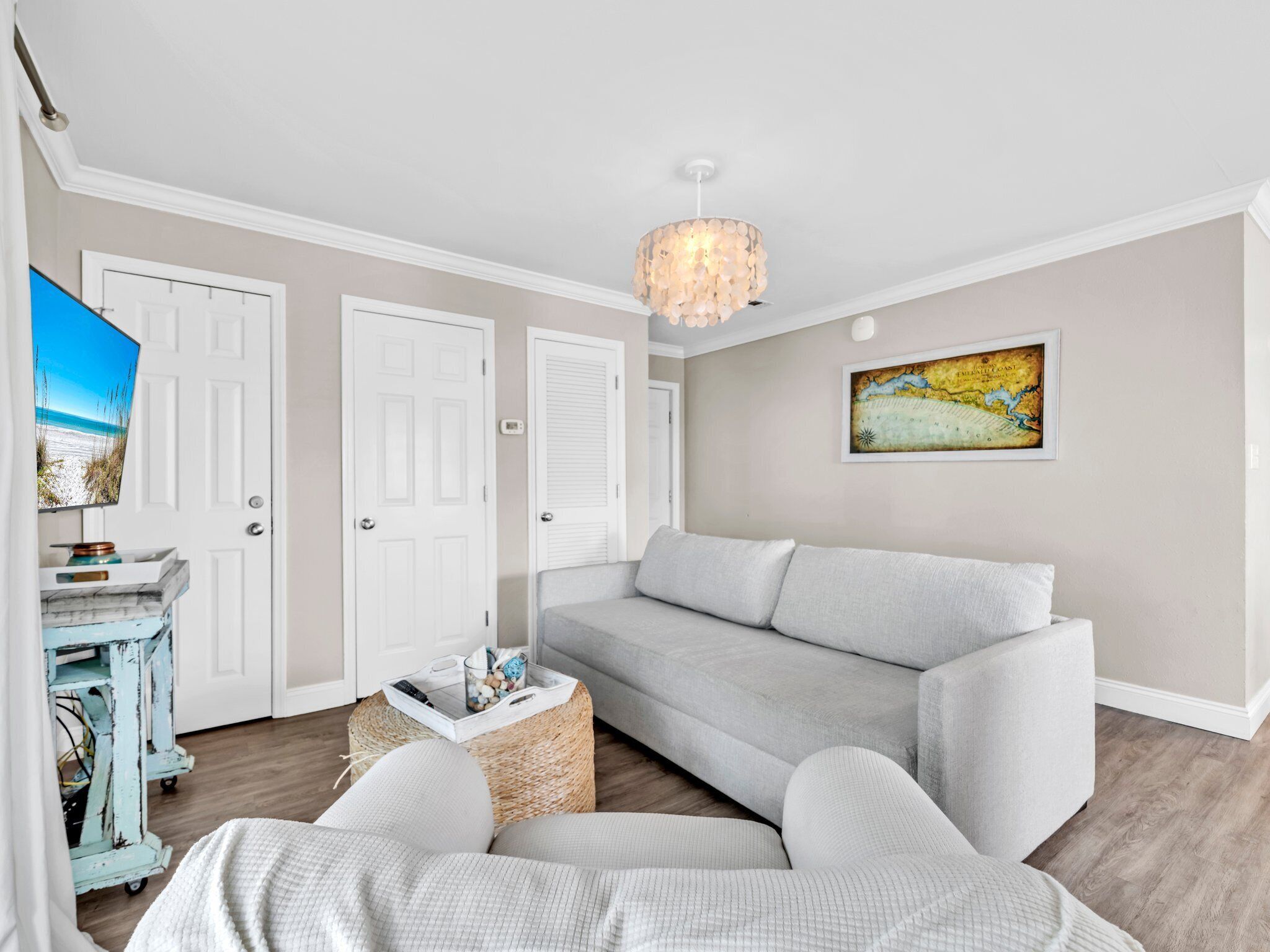A living room with a grey sofa, a television on a stand, a chandelier, and a map on the wall.