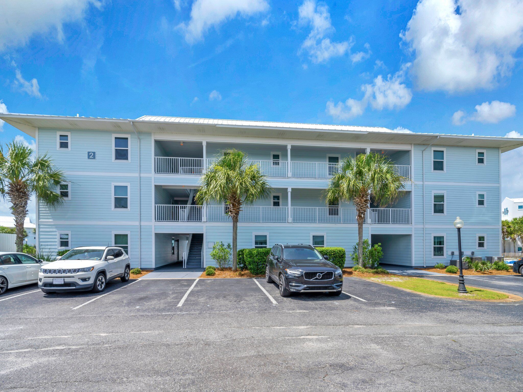 A multi-story hotel with a parking lot, two-story balconies, and palm trees.