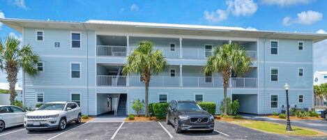 A multi-story hotel with a parking lot, two-story balconies, and palm trees.