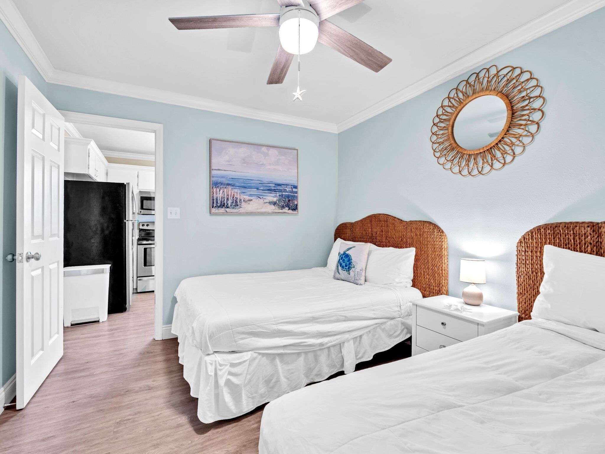 A bedroom with two beds, a ceiling fan, a painting, and a decorative mirror.