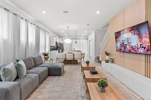 Una sala moderna con un sofá seccional gris, una mesa de centro de madera y un televisor montado en la pared.