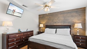 A bedroom with a wooden headboard, a large bed, two bedside tables with lamps, a dresser, and a ceiling fan.