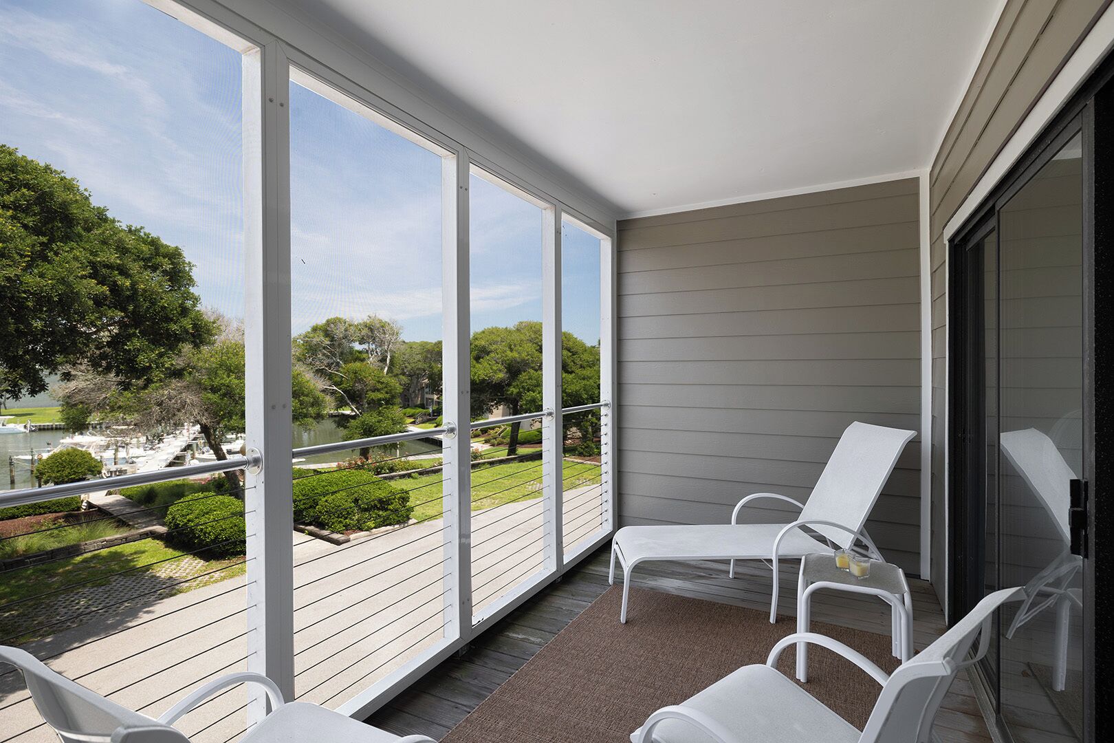 A balcony with white chairs, a view of a lake, and a grassy area with trees.