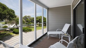 A balcony with white chairs, a view of a lake, and a grassy area with trees.