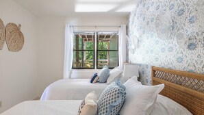 A bedroom with two beds, white bedding, and a window with a view of greenery.