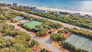 An aerial view of a coastal property with a tennis court, a swimming pool, and a beach.
