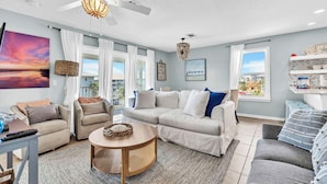 A spacious living room with a large window, a ceiling fan, and a round coffee table.