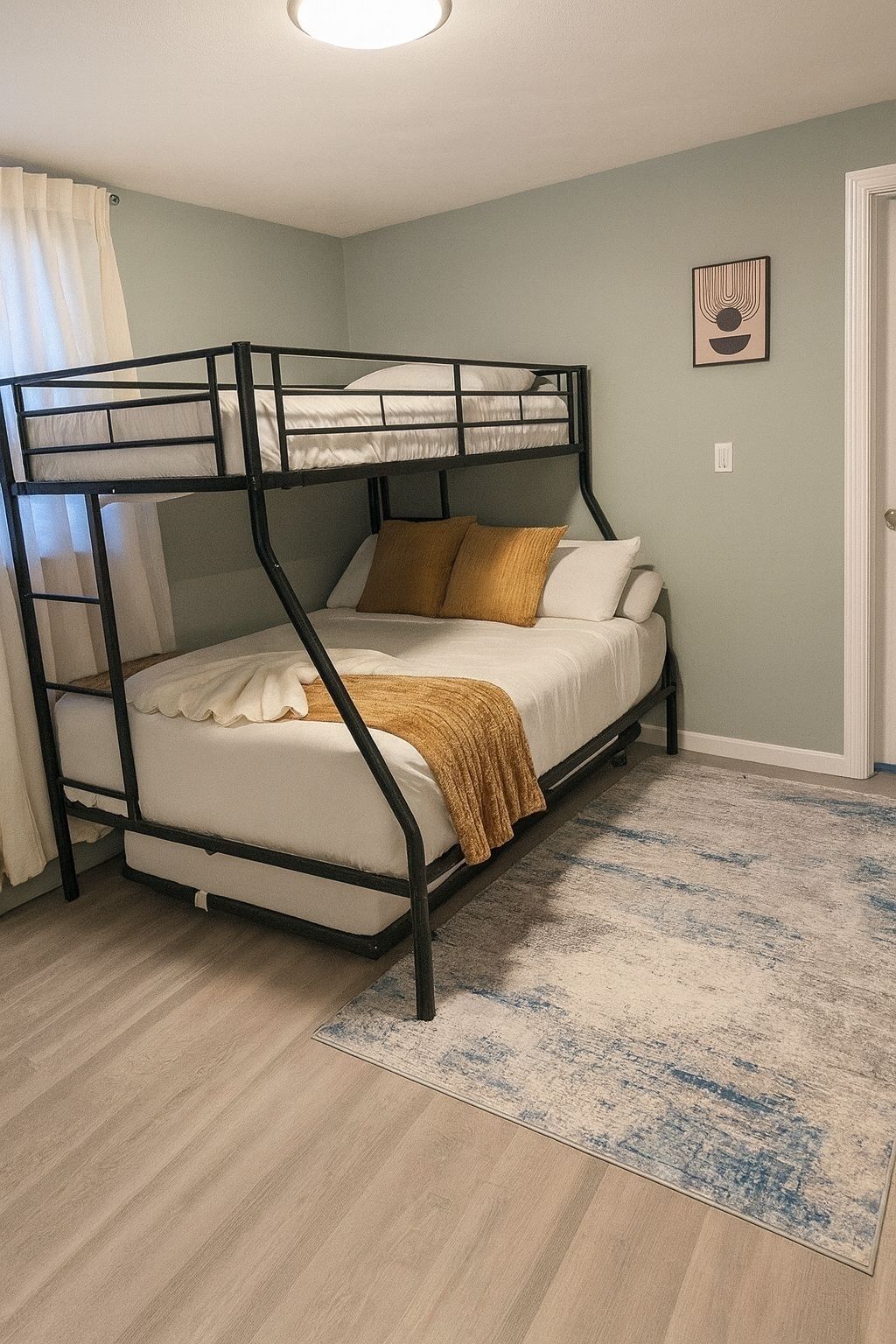Una cama litera con colchón blanco y manta color mostaza, una alfombra color beige y un cuadro en la pared.